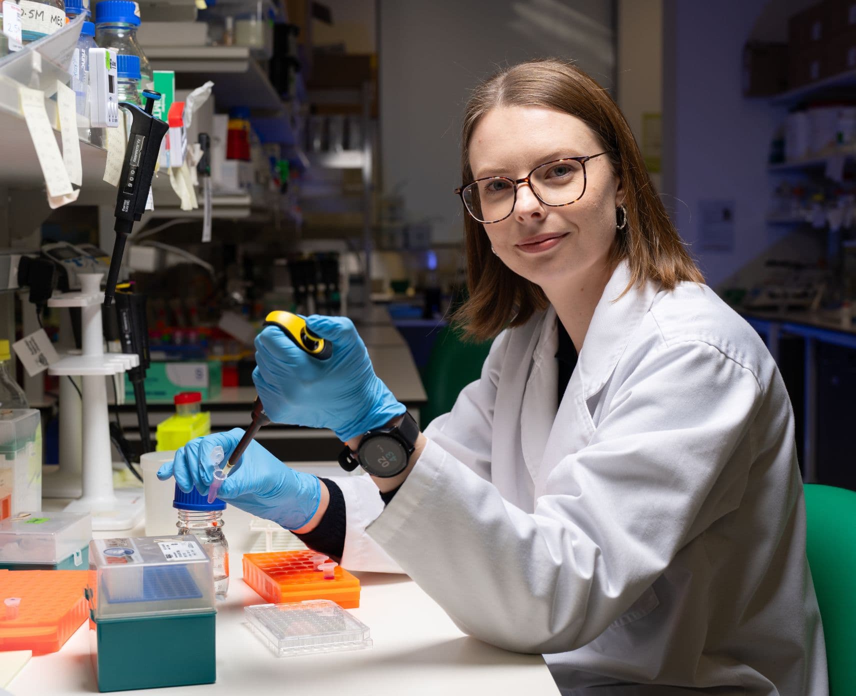 Female scientist holding a pipette, looks at the camera.